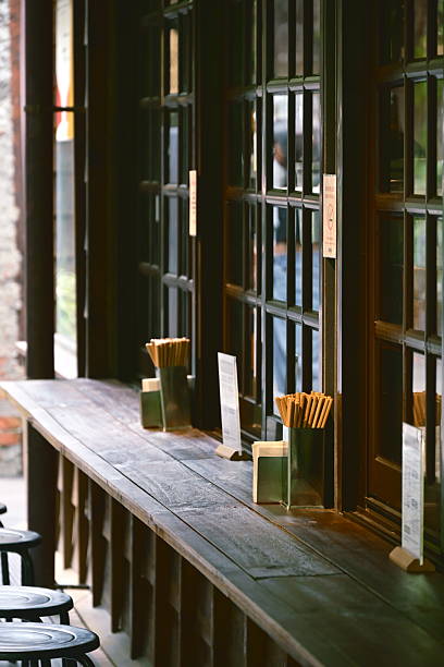 Taiwan - Sep 14, 2025: Outdoor dining wooden bar counter extends along multi-panel wood frame windows, featuring bamboo containers with chopsticks and dark atmospheric lighting.