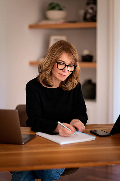 istock Blond haired woman sitting at desk and using laptop and writing something 2235557646