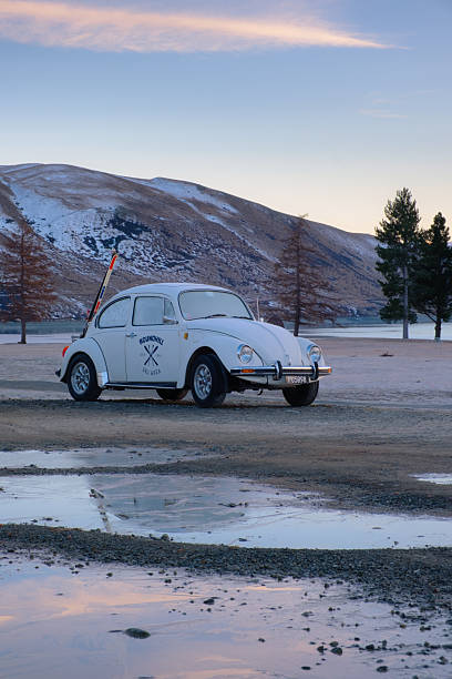 Tekapo, New Zealand - August 16, 2025: An icy dawn on New Zealand's South Island. A classic yet frosty VW Beetle is parked up on the shores of Lake Tekapo, one of the tourist hotspots of the region. A pair of skis is fastened to the back of the car.
