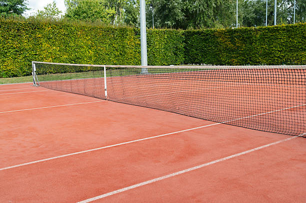 istock Tennis court with a net on a clay surface, surrounded by lush greenery for an inviting atmosphere 2235559913