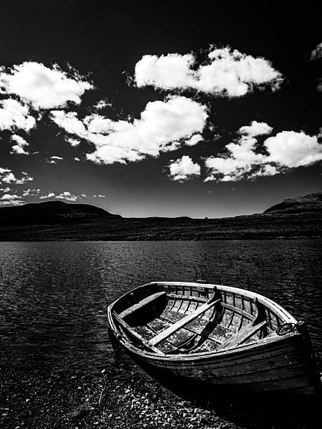 A wooden boat rests on the clear water edge of a mountain lake, monochrome shades enhance texture, silence and atmosphere, offering a timeless sense of solitude and contemplation.