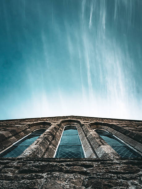 A majestic stone church facade reaches skyward, captured from a low angle with a dramatic wide lens. The composition emphasizes grandeur, symmetry, and timeless architecture beneath a vivid sky.