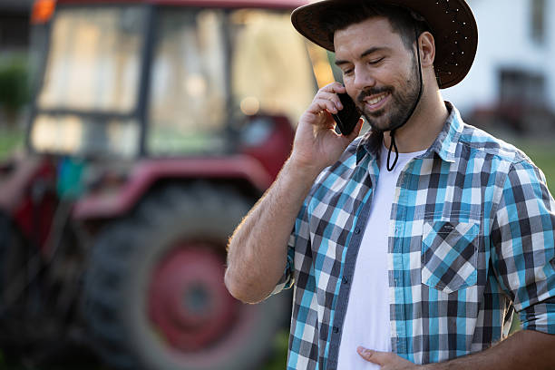 istock Smiling man using smartphone on farm with tractor nearby 2235568807