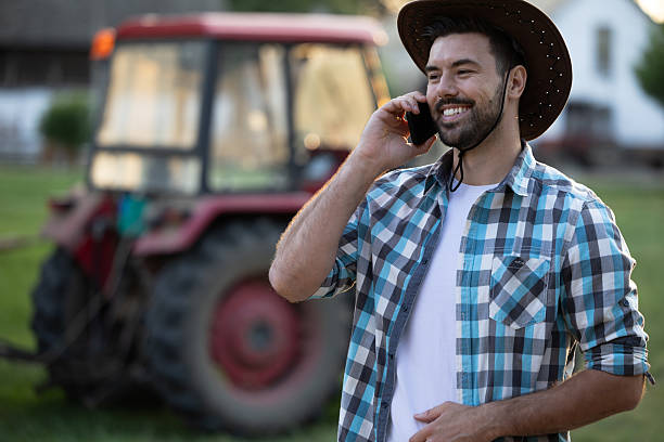 istock Smiling man using smartphone on farm with tractor nearby 2235568952
