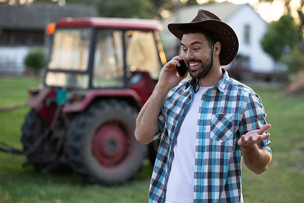 istock Smiling man using smartphone on farm with tractor nearby 2235569038