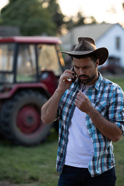 istock Farmer using smartphone in farm setting with tractor nearby 2235569381