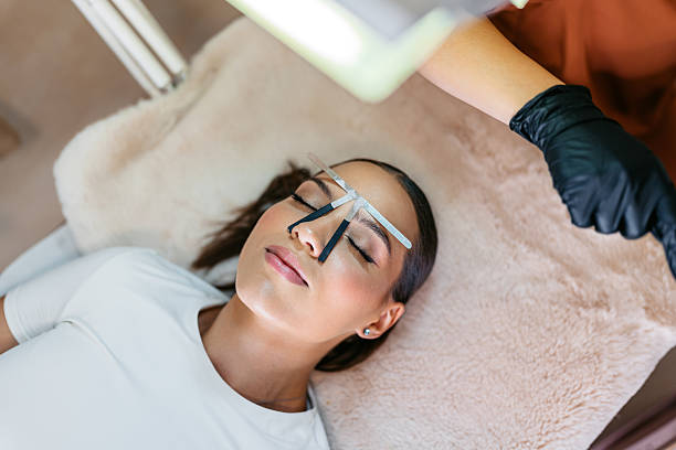 Young woman getting her eyebrows shaped by a female eyebrow technician at a beauty salon.