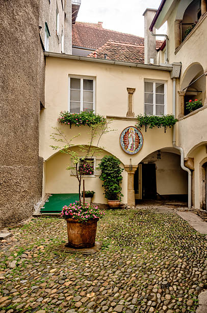 istock A quiet inner courtyard with cobblestone paving, arched entryways, and religious iconography, adorned with potted flowers and greenery in the historic city center. 2235572922