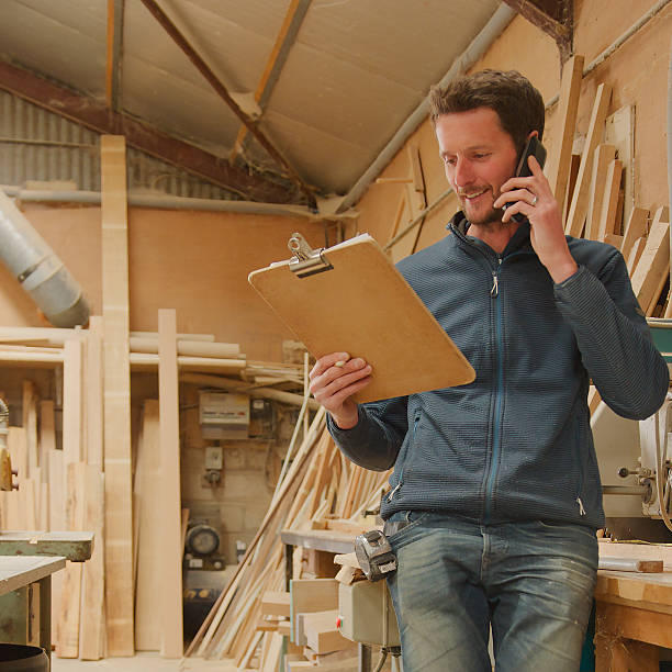 istock Carpenter Working In Woodwork Workshop Making Call On Mobile Phone Whilst Looking At Clipboard 2235577462