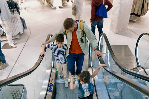istock Father guiding children up escalator in retail store 2235579232
