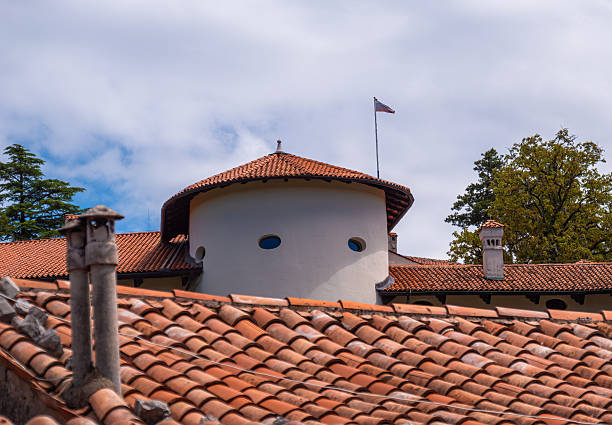 Stanjel, Slovenia - 27 July, 2025: A historic building with a round tower and red-tiled roof under a cloudy sky.