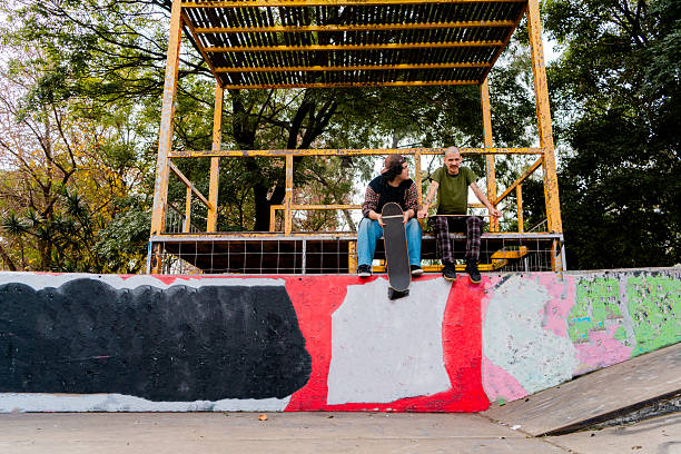 Two friends relax on the skatepark, holding their skateboards and sharing laughs. A laid-back moment that highlights friendship beyond the sport