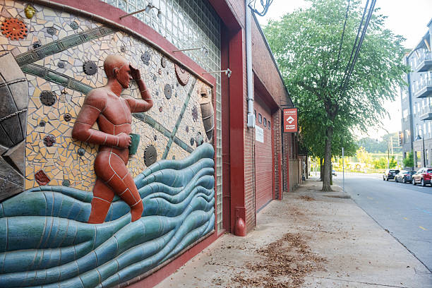 Asheville, United States: July 2, 2025 - A downtown ceramics studio displays a unique wall relief sculpture with a male figure holding a mug on their exterior wall.