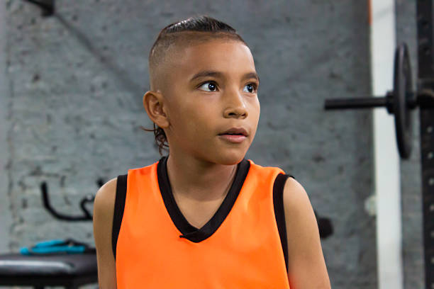 Portrait of a cute Colombian boy wearing an orange jumpsuit doing a strength training routine inside a gym in Neiva, Huila, Colombia