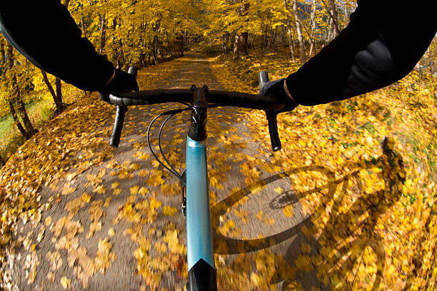 The handlebar view of an autumn road bike ride and the rider's shadow near Nelson, British Columbia, Canada. The cyclist is riding a gravel road bike on a quiet country road. Gravel bikes are like road bicycles but have sturdy wheels and tires for riding on rough terrain.