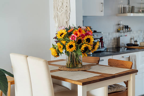 istock Stylish modern interior of open space white kitchen with huge multicolor summer flower bouquet in vase on wooden kitchen counter table, macrame on the wall. Cozy Design home decor. Selective focus. 2235590406
