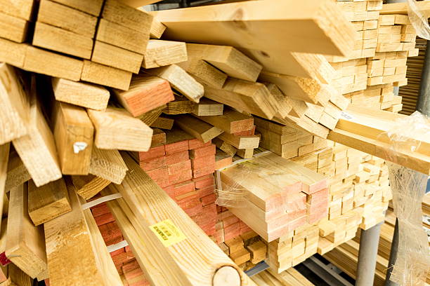 Various wooden planks are stacked neatly in a construction supply store with different sizes and textures, showcasing materials available for building and crafting projects.