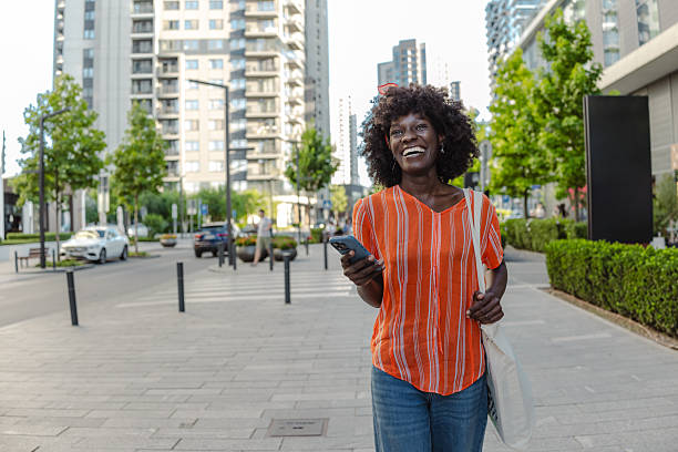 istock Smiling woman in urban setting using phone and carrying reusable bag 2235591858