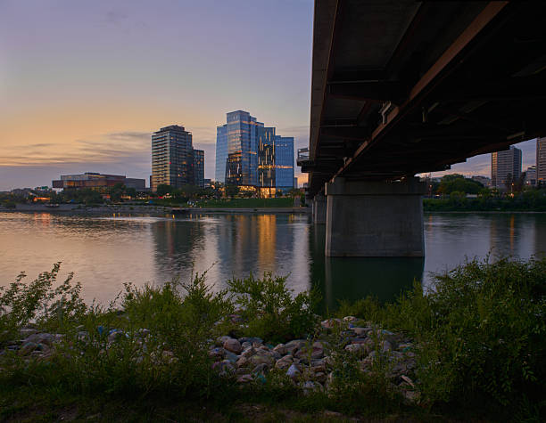 Saskatoon skyline view at twilight with modern high-rise buildings framed by trees and park greenery.
