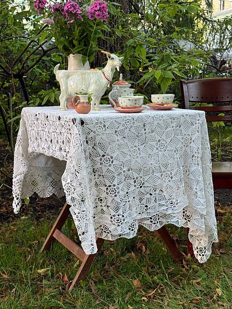 Lace tablecloth draped over table with teapot and cups in garden setting. Mobile photo