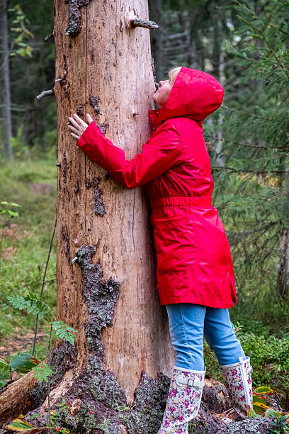 istock A middle-aged Caucasian woman in a red coat hugs a tree trunk. 2235594652