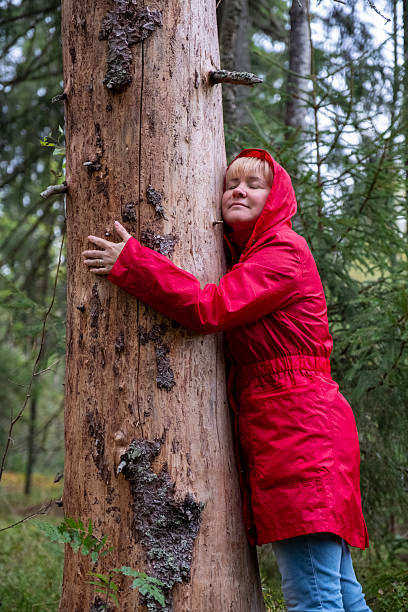 istock A middle-aged Caucasian woman in a red coat hugs a tree trunk. 2235594897
