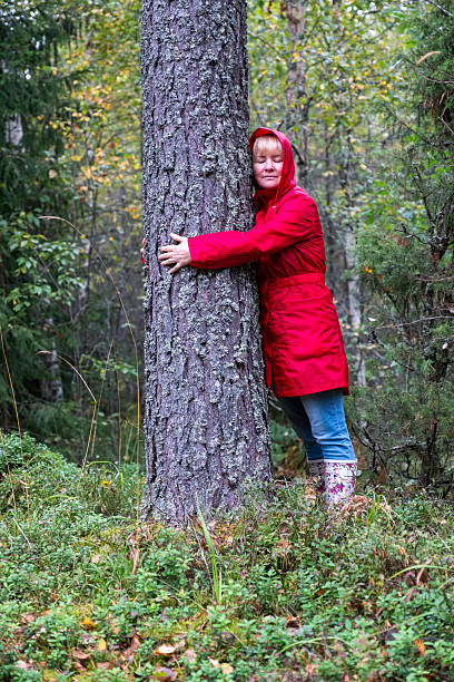 istock A middle-aged Caucasian woman in a red coat hugs a tree trunk. 2235595069