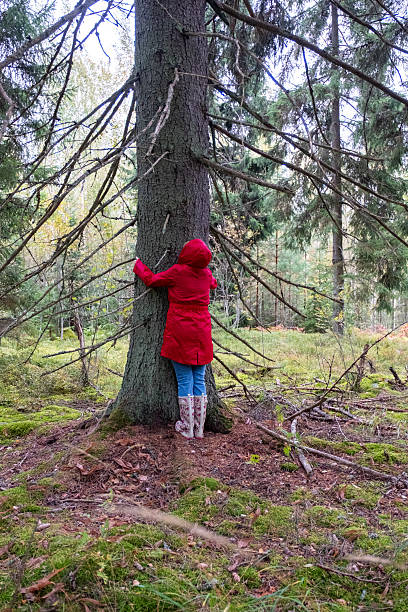 istock A middle-aged Caucasian woman in a red coat hugs a tree trunk. 2235595197