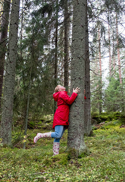 istock A middle-aged Caucasian woman in a red coat hugs a tree trunk. 2235595213