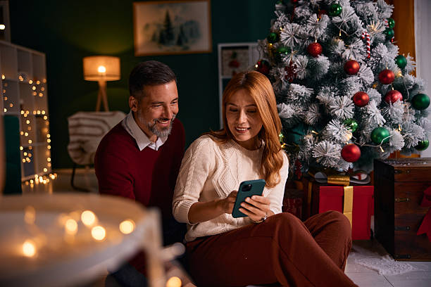 istock Couple looking at smartphone sitting by Christmas tree 2235596025