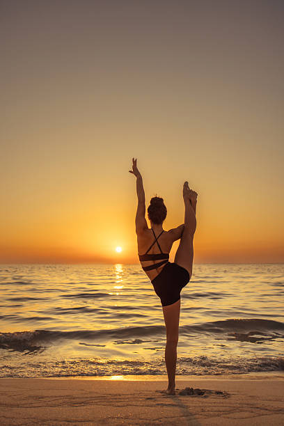 A person balances in a yoga pose on a sandy beach, facing a mesmerizing ocean sunset. The tranquil atmosphere highlights wellness, mindfulness, and connection with nature, capturing the essence of calm and balance.