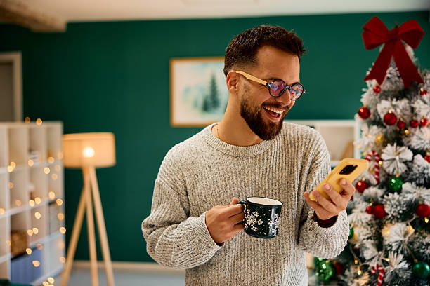 Young man using phone and drinking coffee during Christmas holidays