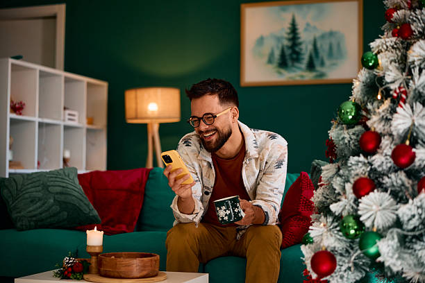 istock Young man using phone and drinking coffee during Christmas holidays at home 2235599405