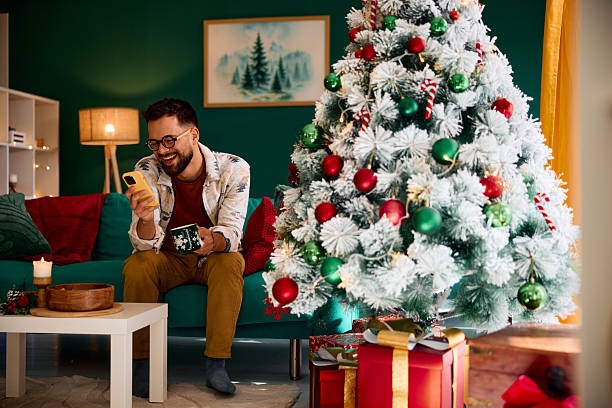 istock Young man using phone and drinking coffee by the Christmas tree 2235599443