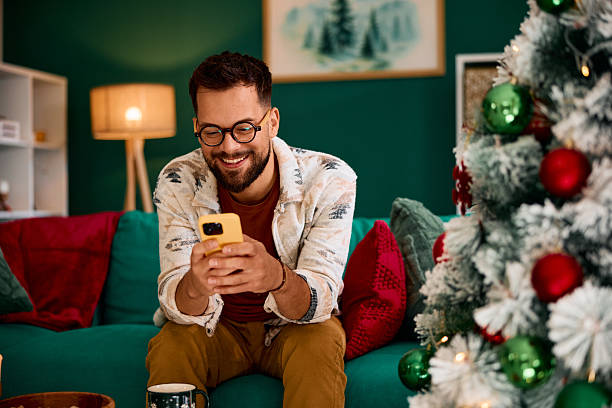 istock Young man using smartphone on Christmas day sitting on the sofa 2235599463