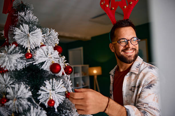 istock Young man decorating Christmas tree wearing reindeer antlers 2235599711
