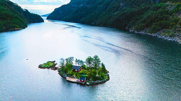 Experience the beauty of Lovrafjorden in Norway, where a picturesque cabin rests on a small island, embraced by peaceful waters and lush green surroundings, creating a serene escape in nature.