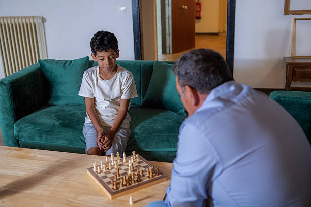 A grandfather and grandson enjoy a quiet game of chess together in a cozy, well-decorated living room.