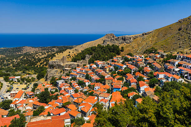 Traditional village with red roofs and castle ruins on a green hillside above the deep blue sea under a clear summer sky.