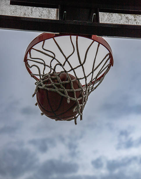 Upshot of basketball swooshing though net against a moody sky