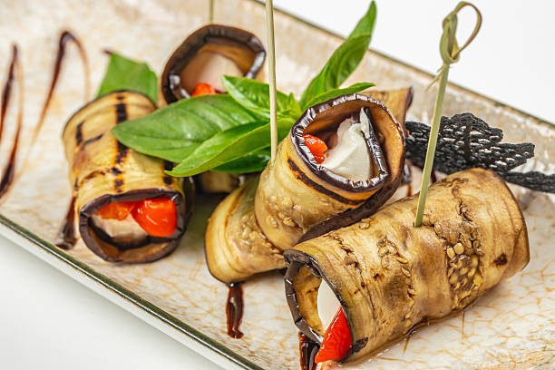 Grilled eggplant rolls stuffed with cheese and red peppers on a ceramic plate. top view.