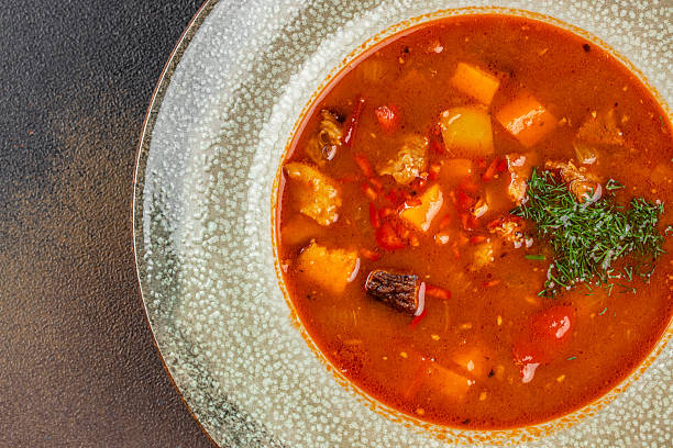 Traditional goulash soup with beef, vegetables, potatoes, and fresh herbs in a ceramic bowl. copy space, top view