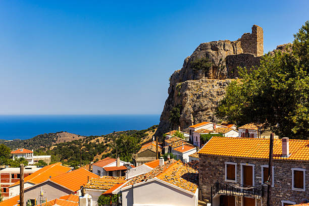 Samothraki, Greece  Coastal village with orange rooftops and stone buildings beneath a rocky hill crowned by ancient fortress ruins, overlooking the deep blue Aegean Sea.