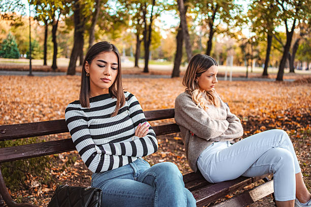 istock Two young women having an argument while sitting on a bench in a park during autumn 2235613854