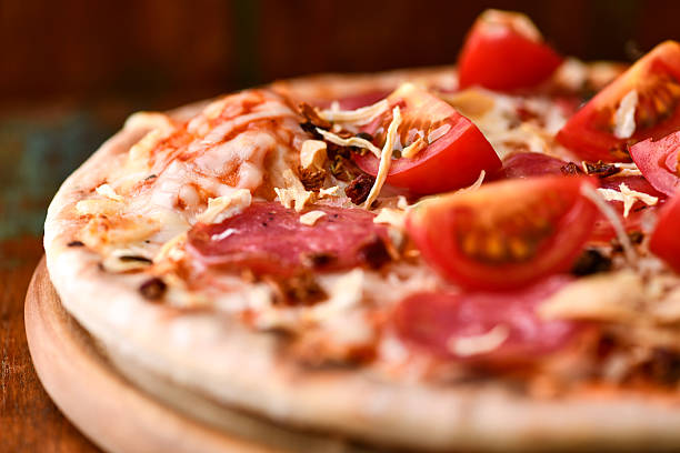 Pizza with ham, salami, cherry tomatoes and mozzarella cheese. Rustic wooden background. Soft focus. Close up.