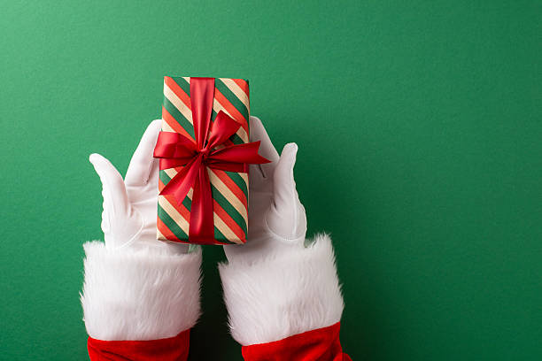 istock Santa's gloved hands present a festive wrapped gift with a bright red ribbon on a green backdrop, symbolizing Christmas celebrations, gift exchange, seasonal joy, and traditional holiday imagery 2235616881
