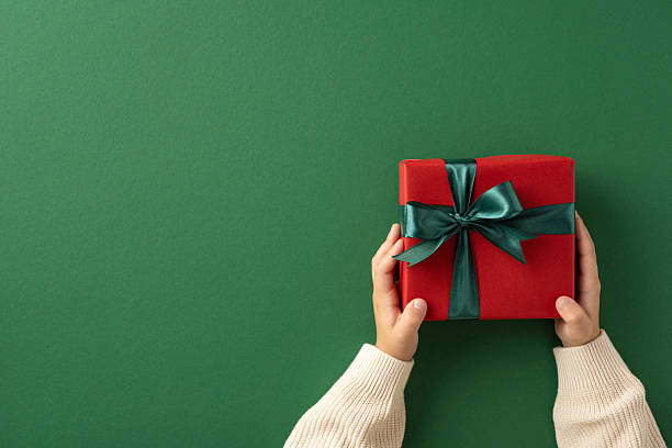 istock Hands holding a decorated gift wrapped with ribbon on a green background 2235616903