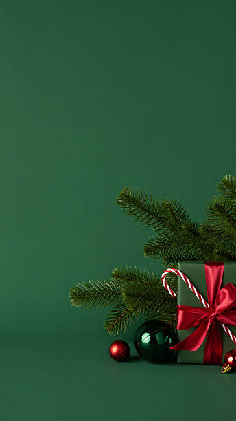 Green vertical background featuring a Christmas gift box, ornaments, and pine branches for festive themes