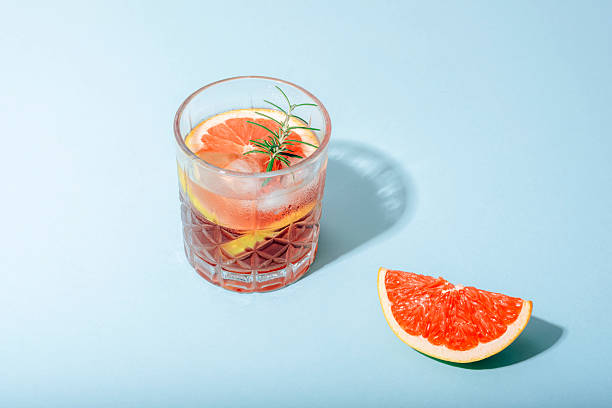 istock Glass of grapefruit cocktail with fruit slices and rosemary on blue background with sharp shadows. Closeup 2235618048