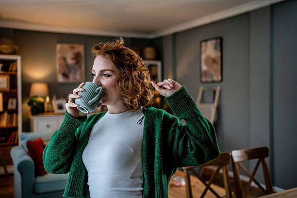 istock Young woman drinking tea and stretching at home 2235628089